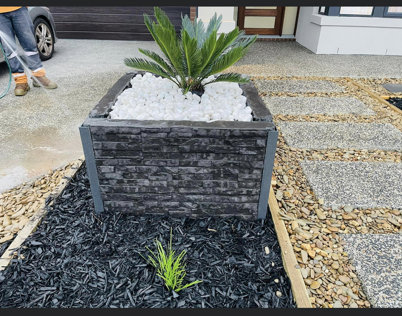 Stacked stone planter box with a cycad and black mulch bed